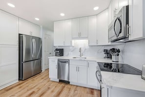 A modern kitchen with white cabinets, stainless steel appliances, a dishwasher, and a microwave. - Tide Time Oceanfront at Sea Cabin w Pool (North Myrtle Beach)
