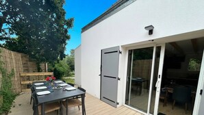 A patio with a table set for dining, a sliding glass door leading to an interior space, and a wooden fence in the background. - Ty Argoat -  Your haven between land and sea (Plouarzel)