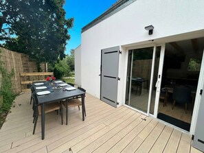 A patio with a table set for dining, a sliding glass door leading to an interior space, and a wooden fence in the background. - Ty Argoat -  Your haven between land and sea (Plouarzel)