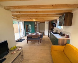 Een moderne keuken met houten balken, een eethoek met een tafel gedekt voor vier personen, en een gele bank.
