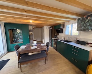 Een knus keuken met houten balken, een eethoek met een tafel voor vier personen, en een groene accentmuur.