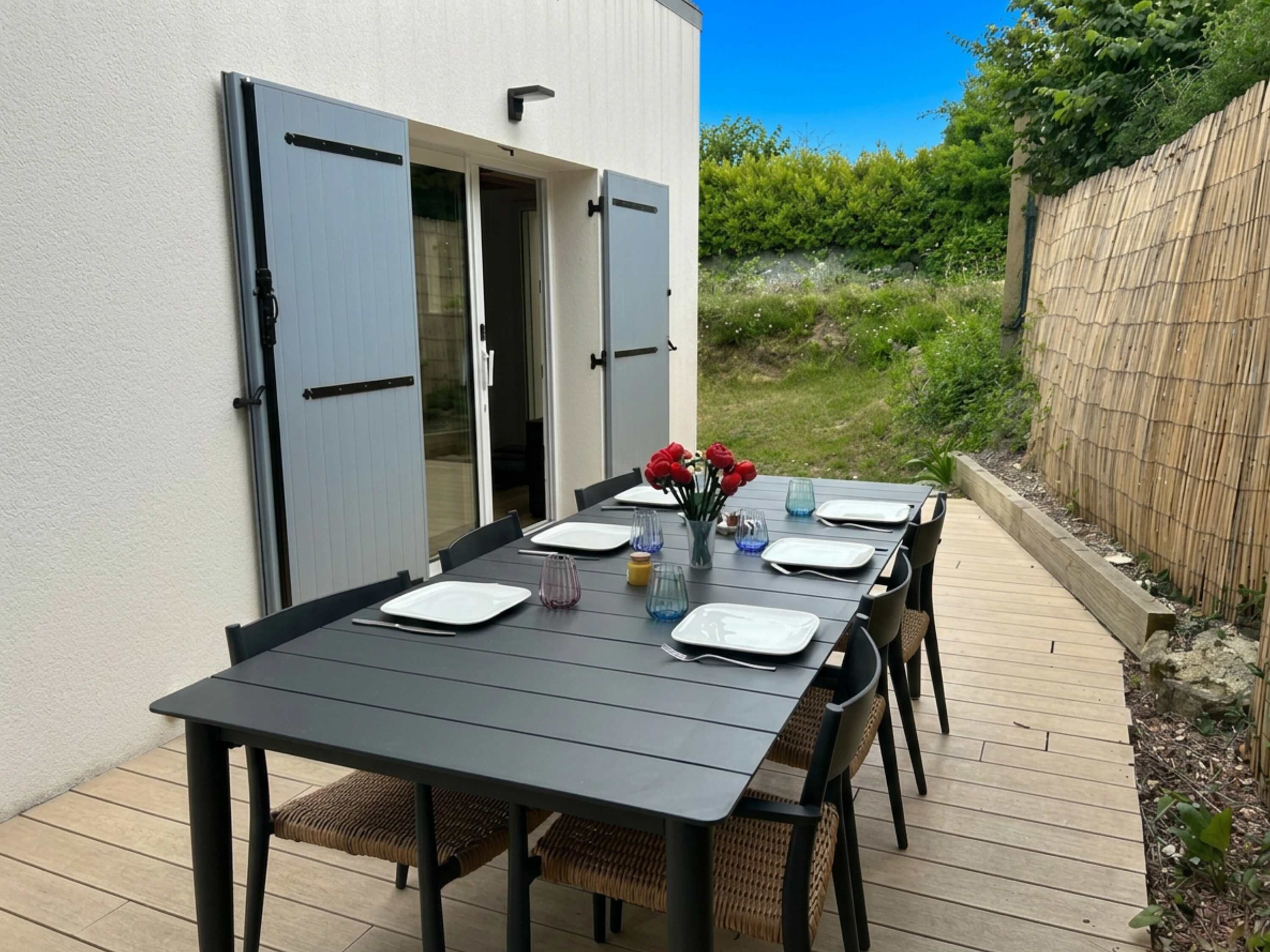 A patio table set for four with a view of a garden and a wooden fence.