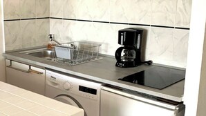 A kitchenette with a coffee maker, a dish rack, a dishwasher, and a sink. - 40m² AC Studio with Balcony & Parking (Sanary-sur-Mer)