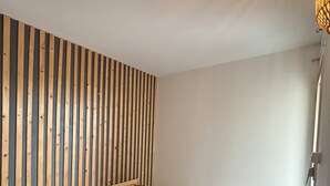 Ein Schlafzimmer mit einem querverlegten Holzkopfteil, einem Einzelbett mit grauer Bettdecke und einer schlichten weißen Wand.