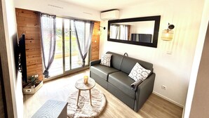 Ein modernes Wohnzimmer mit einem grauen Sofa, einem runden Couchtisch und einem großen Fenster mit Vorhängen.