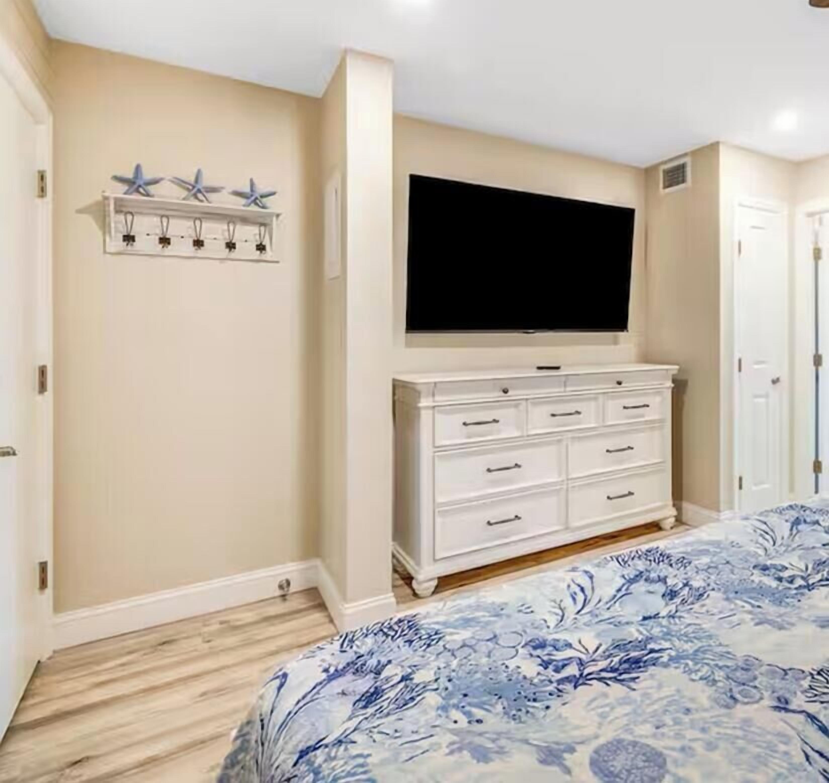 A bedroom with a bed, a dresser, a TV, and a wall-mounted light fixture.