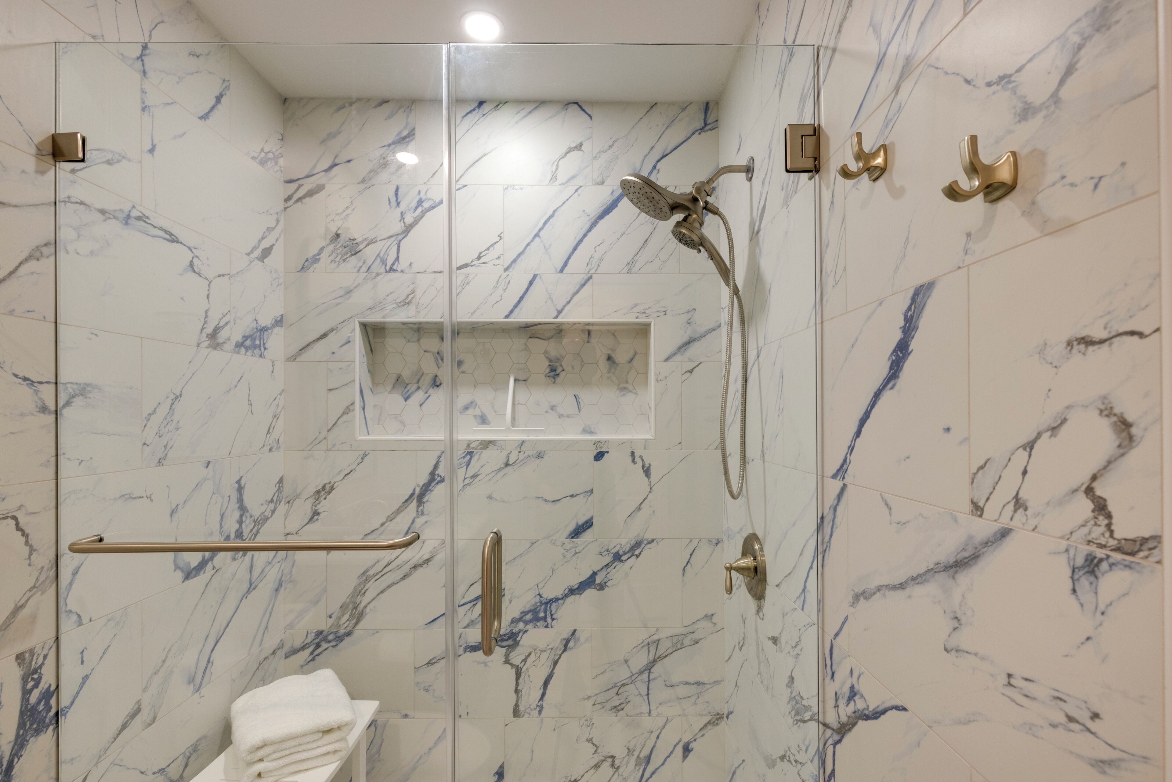 Een moderne badkamer met een douchecabine van glas, marmeren wanden en gouden accessoires.