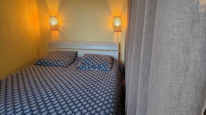 Ein Bett mit gemusterten Bettwaren, zwei Wandleuchten und ein teilweise gezogener Vorhang.