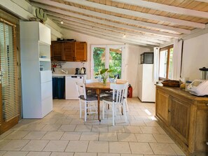 A kitchen with a dining table, chairs, cabinets, and a view of greenery outside. - Rustic house with amazing sea view (Le Pradet)