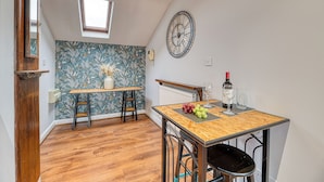 Una cocina con una mesa de madera, sillas, un reloj y una ventana.