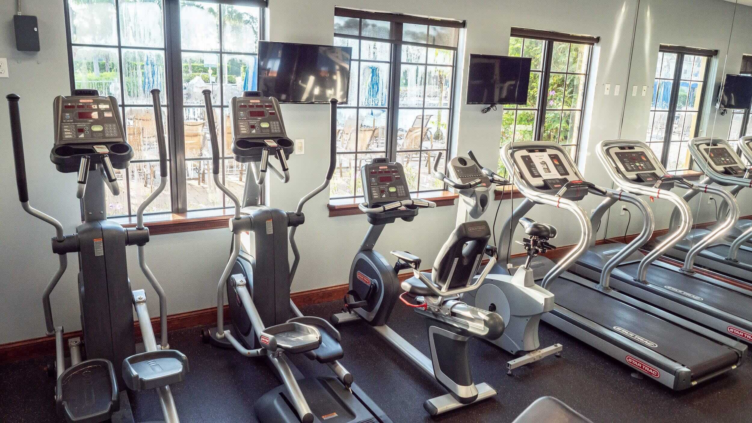 A gym with various exercise machines, large windows, and a treadmill.