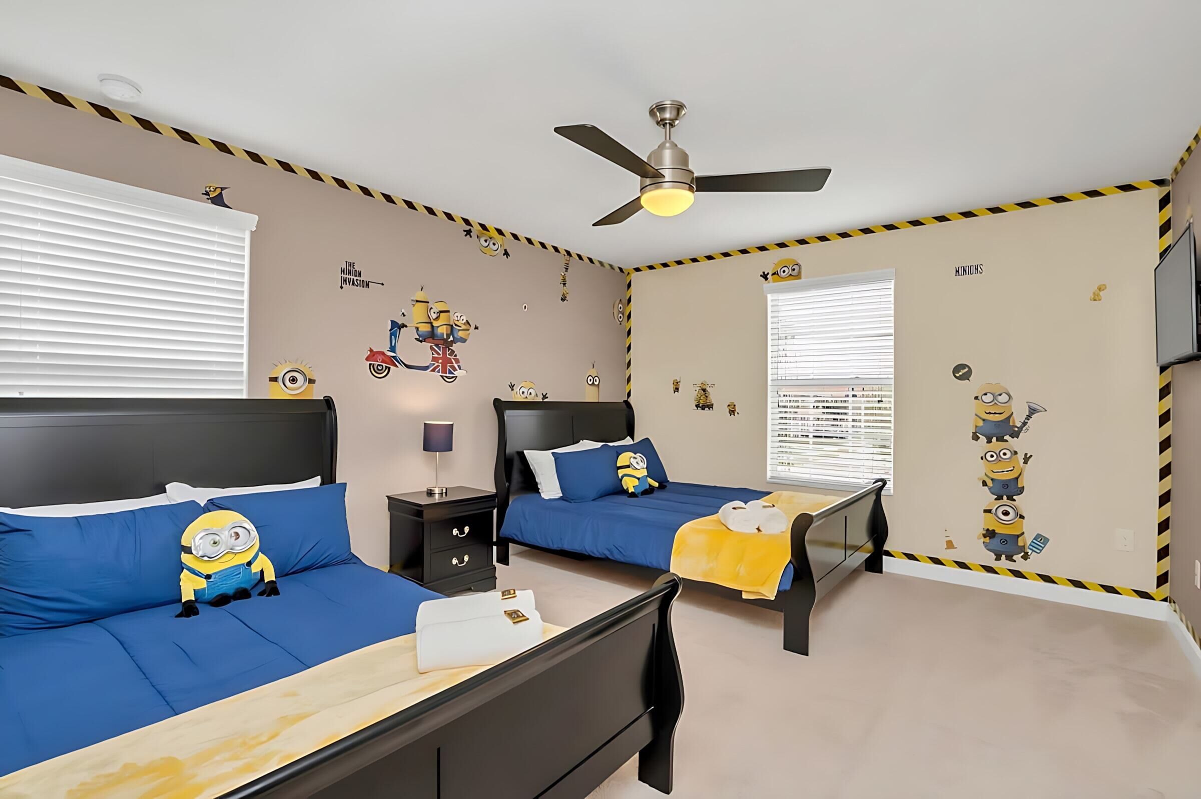 A bedroom with two beds, a ceiling fan, and Minion-themed wall decals.