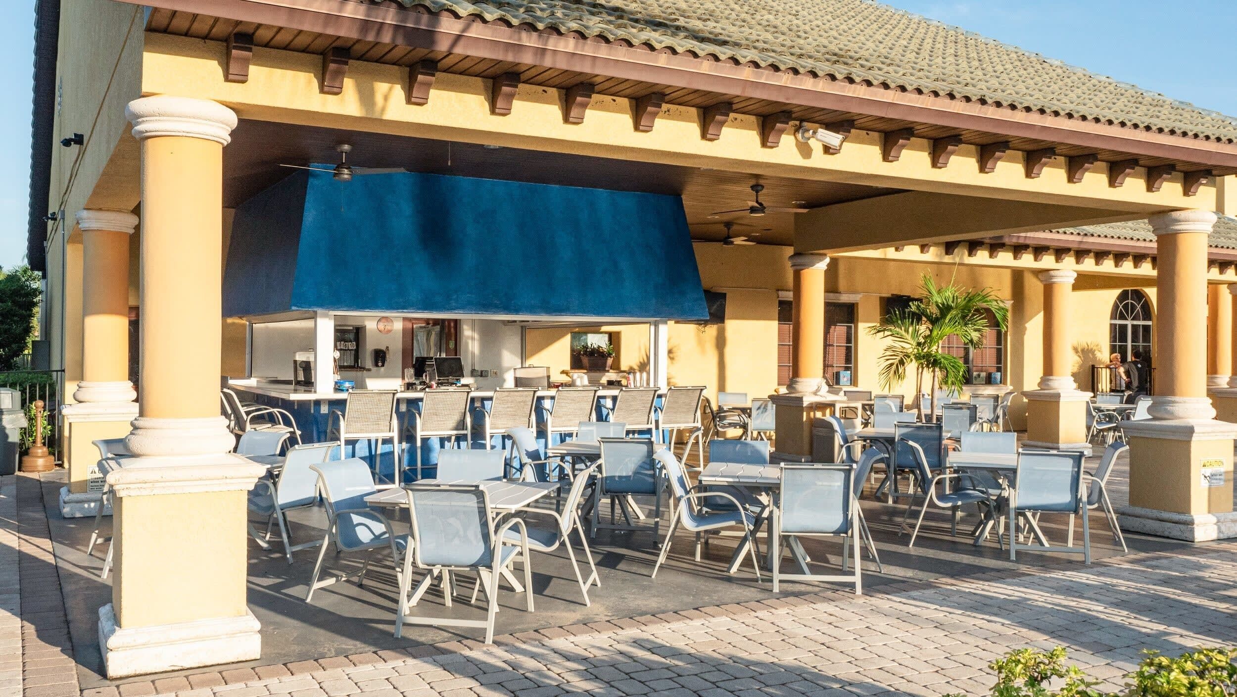An outdoor patio with multiple tables and chairs, a covered seating area, and a building with a tiled roof and columns.