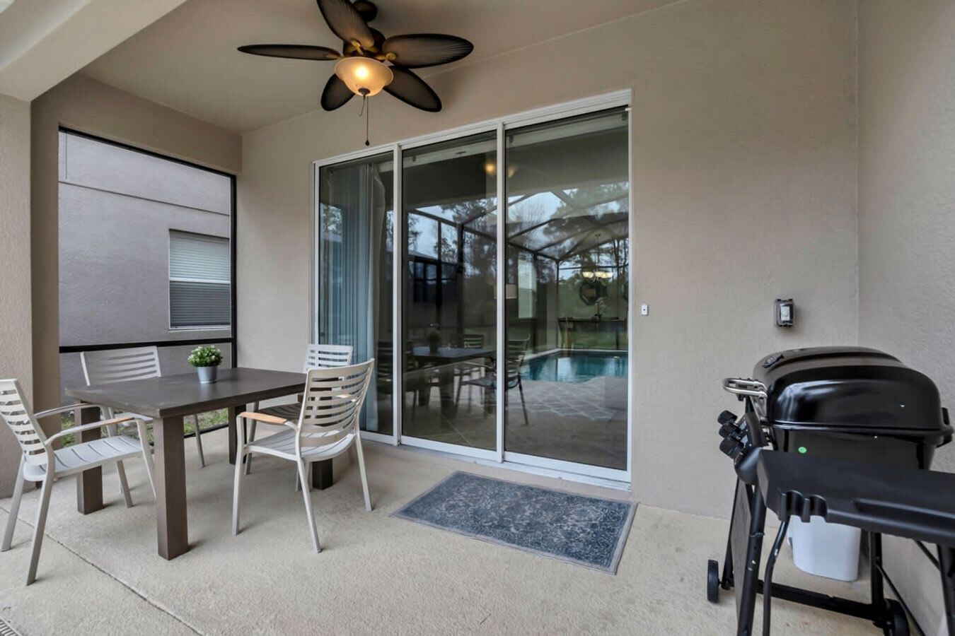 An outdoor patio with a table and chairs, a ceiling fan, and a grill.