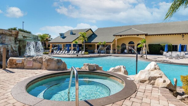 A swimming pool with a hot tub, lounge chairs, and a waterfall feature. - Spacious Family Home w Pool, Hot Tub & BBQ (Kissimmee)