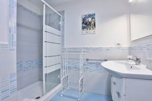 Een badkamer met een douche, een wastafel, een handdoekhouder en een poster aan de muur.