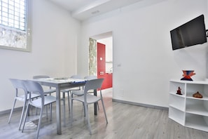 Ein modernes Zimmer mit Esstisch, Stühlen, Fernseher und Bücherregal.