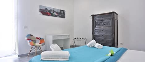 A hotel room with a bed, a desk, a chair, a wardrobe, and a cityscape painting on the wall.