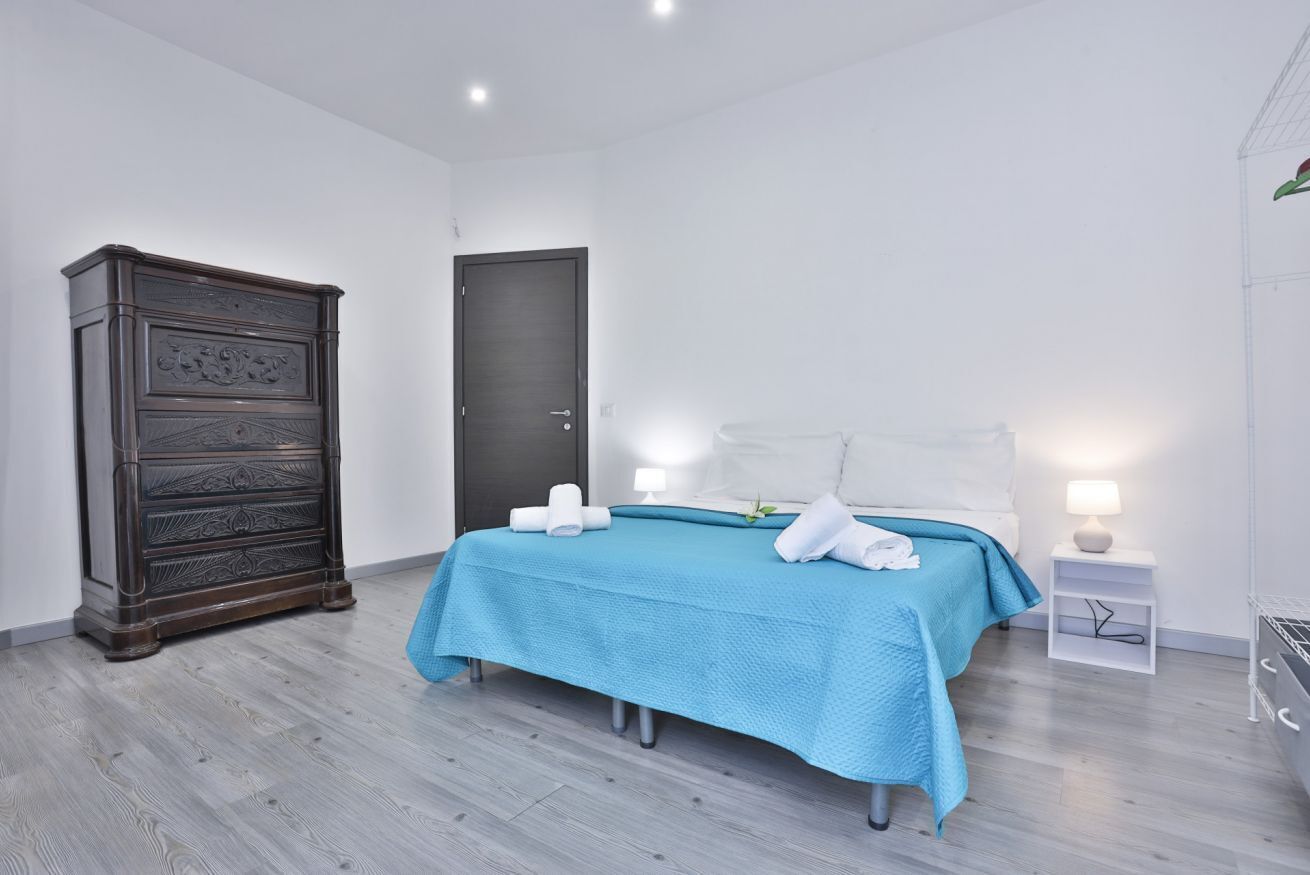 Quarto com cama, guarda-roupa, porta e mesa de cabeceira com abajur.