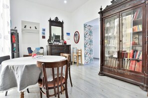 Een eetgedeelte met een ronde tafel, stoelen, een kast met glazen deuren en een wand met planken en een spiegel.