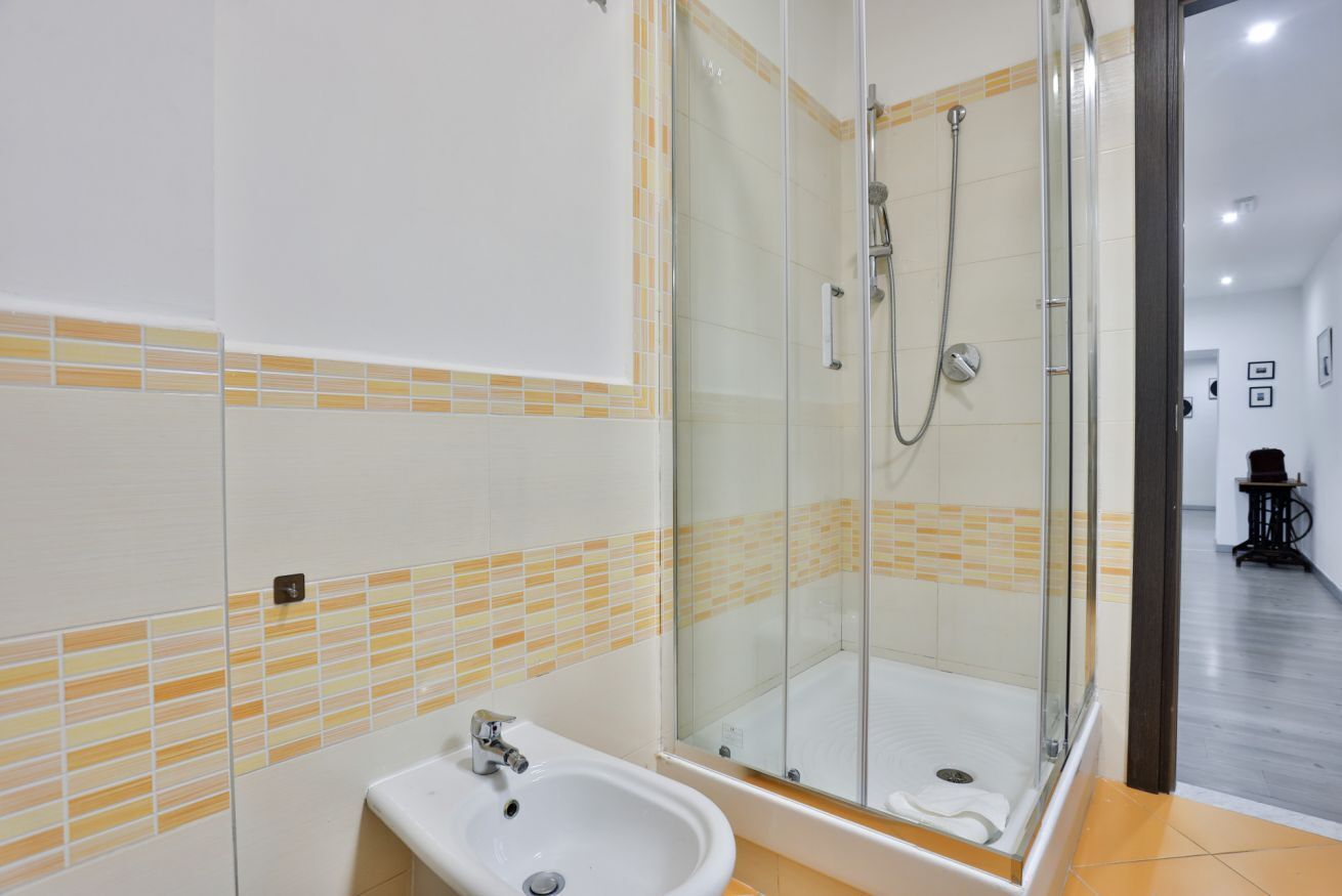 A modern bathroom with a glass-enclosed shower, a sink, and a tiled floor.