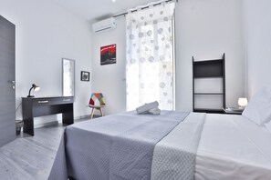 Een moderne slaapkamer met een bed, een bureau, een stoel, een nachtkastje en een raam met gordijnen.