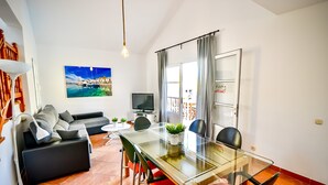 A modern living room with a glass dining table, black and red chairs, a black sofa, a flat-screen TV, and a large painting of a coastal scene. - Casa Culwick - Villa in Gran Canaria with Swimming Pool (Mogán)