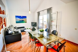 Ein modernes Wohnzimmer mit einem Glastisch, schwarzen und roten Stühlen, einem schwarzen Sofa, einem Flachbildfernseher und einem großen Gemälde einer Küstenlandschaft.