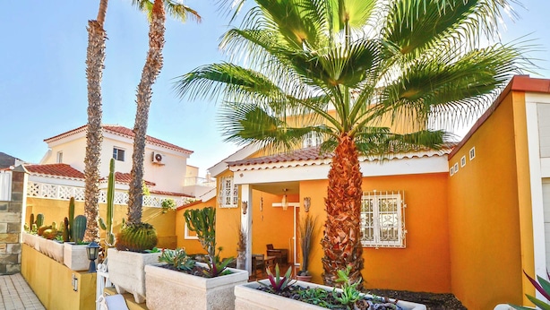 A residential building with a yellow facade, palm trees, and cacti in the courtyard. - Casa Culwick - Villa in Gran Canaria with Swimming Pool (Mogán)