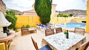 A patio with a pool, outdoor seating, and a table with a bottle. - Casa Culwick - Villa in Gran Canaria with Swimming Pool (Mogán)