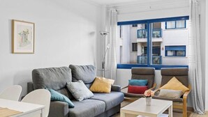 En stue med sofa, to lænestole, sofabord, gulvlampe og et vindue med udsigt til en bygning.