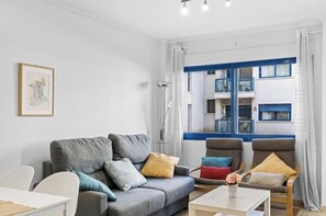 A living room with a sofa, two armchairs, a coffee table, a floor lamp, and a window with a view of a building. - Apartment with Private Swimming Pool and Jacuzzi in Alicante Hills (Aliante)