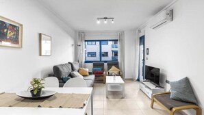 En moderne stue med sofa, sofabord, fjernsyn og et spiseområde med bord og stole.