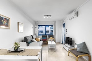 A modern living room with a sofa, coffee table, TV, and a dining area with a table and chairs. - Apartment with Private Swimming Pool and Jacuzzi in Alicante Hills (Aliante)