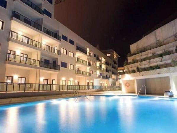 A multi-story hotel with balconies, a swimming pool, and a well-lit exterior. - Apartment with Private Swimming Pool and Jacuzzi in Alicante Hills (Aliante)