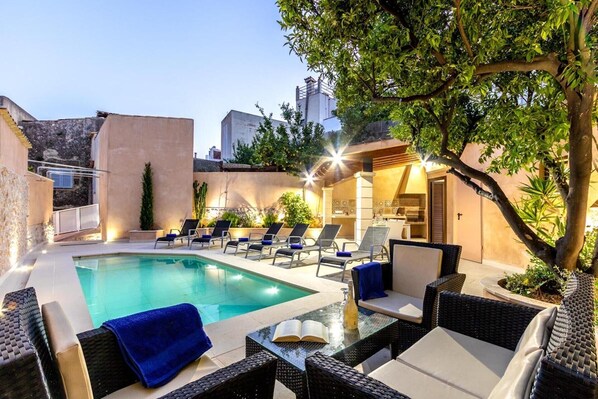 A poolside area with lounge chairs, a table with a book and bottle, and a tree. - Holiday Home "Horta 55" with Pool, Wi-Fi, Air Conditioning, Garden & Terraces (Pollença)