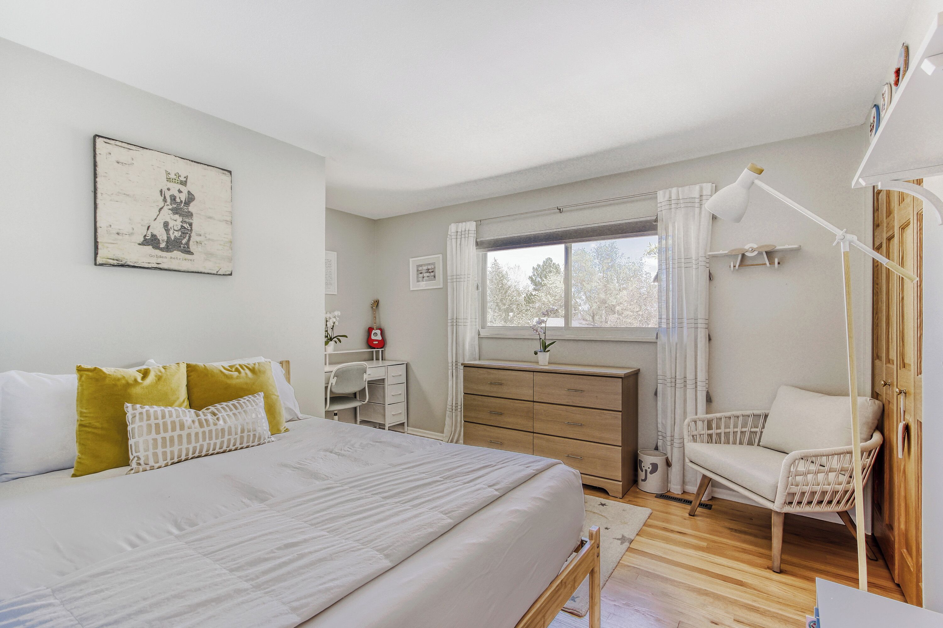 A bedroom with a bed, a desk, a dresser, a chair, and a window with curtains.