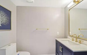 Une salle de bain avec des toilettes blanches, un lavabo doté de robinetterie dorée et un miroir avec un cadre doré.