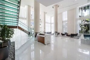 A spacious lobby with a marble reception desk, seating area, and a staircase with glass railings. - > Amazing NEW Remodeled LOFT < (Miami)