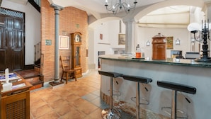 A kitchen with a brick wall, a wooden door, a clock, and a bar area with stools. - Casa Cubo Rural Home H12 – Authentic Charm in Alhama de Granada (Alhama de Granada)