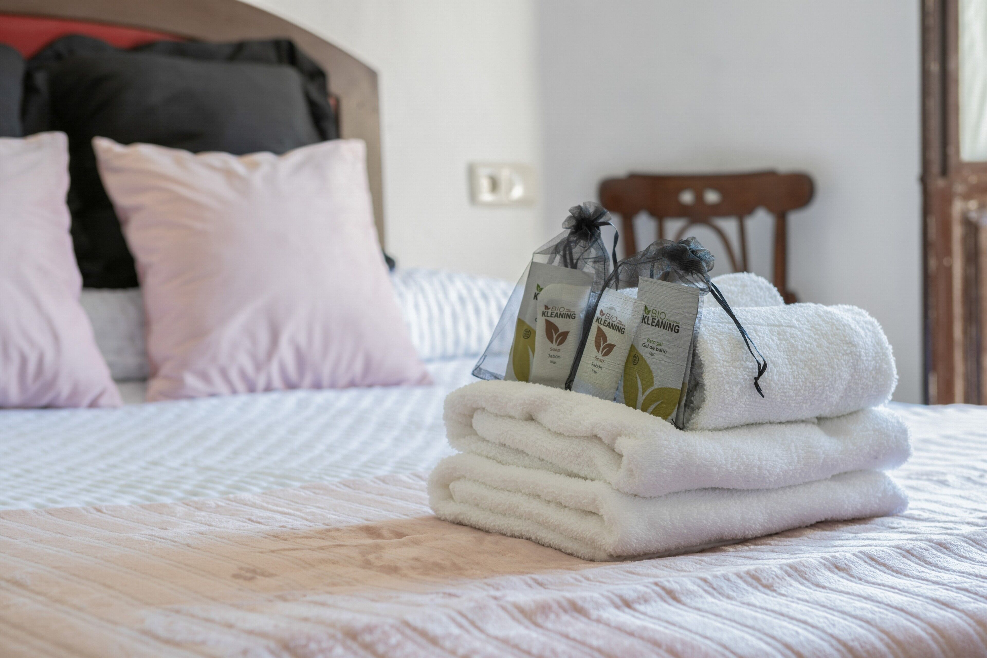 Een net opgemaakt bed met opgevouwen witte handdoeken en twee flessen schoonmaakmiddelen, met een gestreept dekbed.