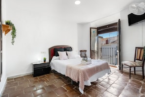 A bedroom with a bed, bedside table, chair, and a balcony view.
