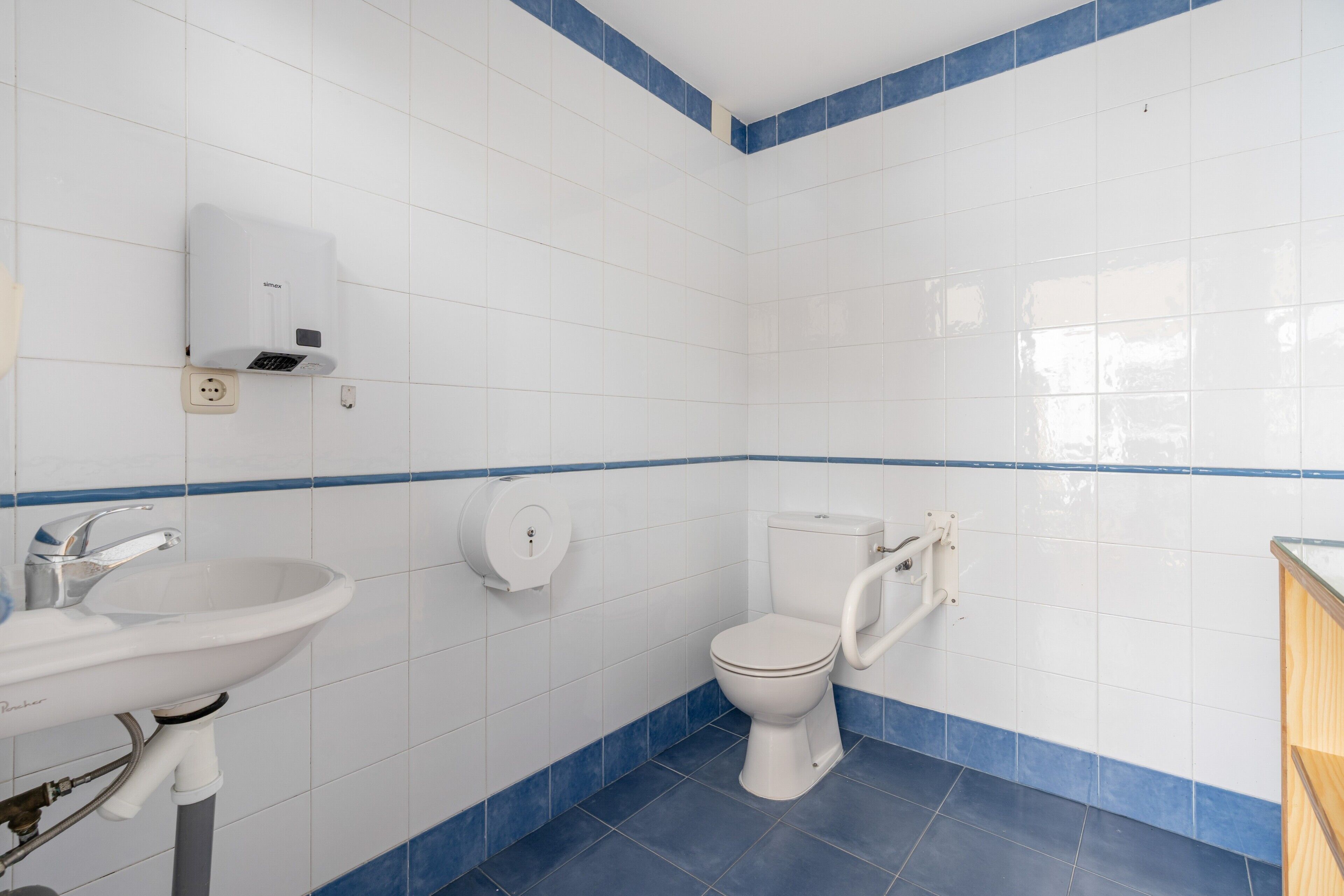 Een badkamer met witte tegels, een wastafel, een toilet en een vloer met blauwe tegels.