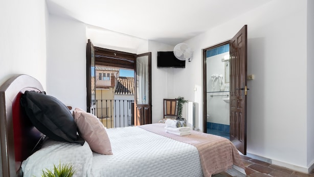 A bedroom with a bed, a potted plant, a TV, and a door leading to a balcony. - Casa Cubo Rural Home H12 – Authentic Charm in Alhama de Granada (Alhama de Granada)