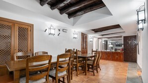 A dining area with wooden furniture, a tiled floor, and a kitchen in the background. - Casa Cubo Rural Home H12 – Authentic Charm in Alhama de Granada (Alhama de Granada)