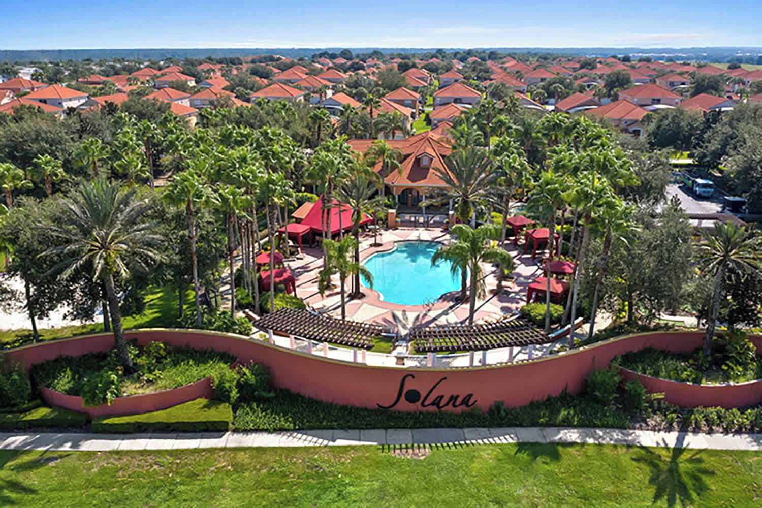 A resort with a central pool, surrounded by palm trees and red-roofed buildings.