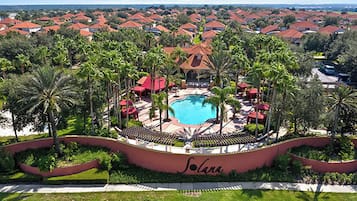 A resort with a central pool, surrounded by palm trees and red-roofed buildings.