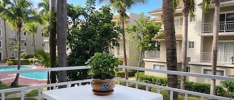 A balcony with a white table and chairs, overlooking a swimming pool and palm trees.
