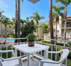 A balcony with a white table and chairs, overlooking a swimming pool and palm trees. - Sol Caribe Sleep&Go (Punta Cana)