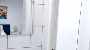 Un baño con un lavamanos blanco, un espejo y una cabina de ducha con mampara de vidrio.